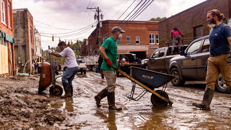 People clean up a muddy downtown street using wheelbarrows