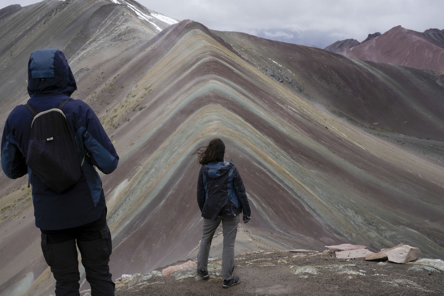 Two people stand at a viewpoint overlooking a striped mountain.