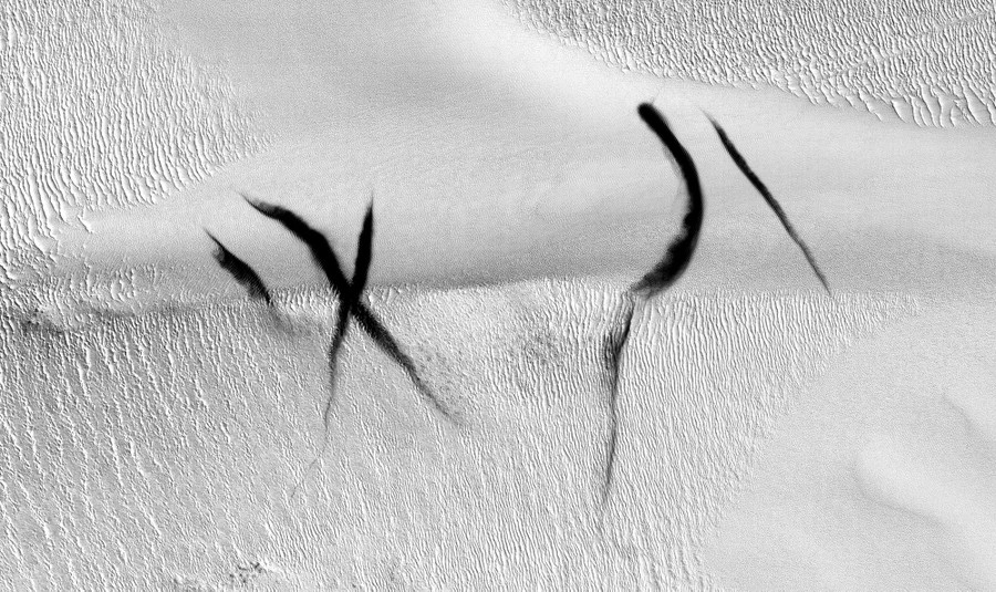Five dark streaks cross a Martian dune, with one pair forming a rough letter "X."