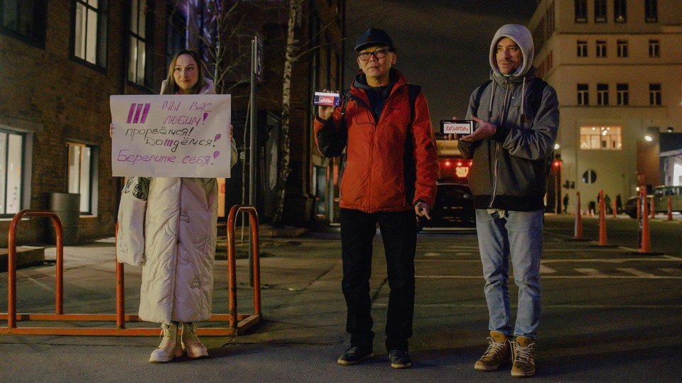 Three people hold up signs on placards and their mobile phones