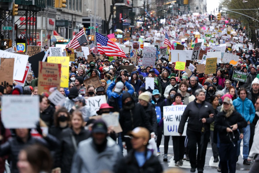 A large crowd of protesters marches down a street in New York City.