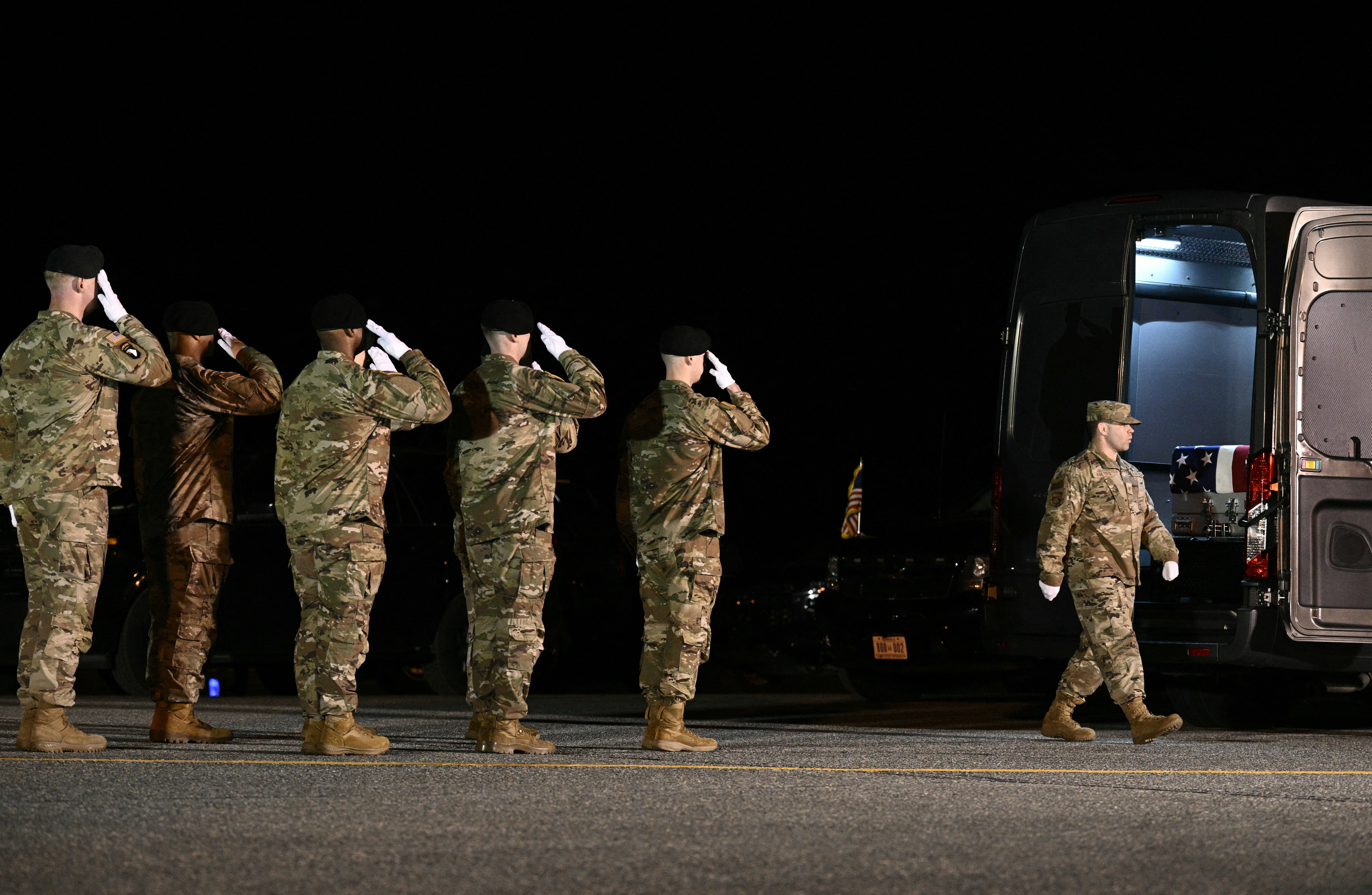 Members of a U.S. Army carry team salute as a flag-draped coffin is moved into a vehicle.