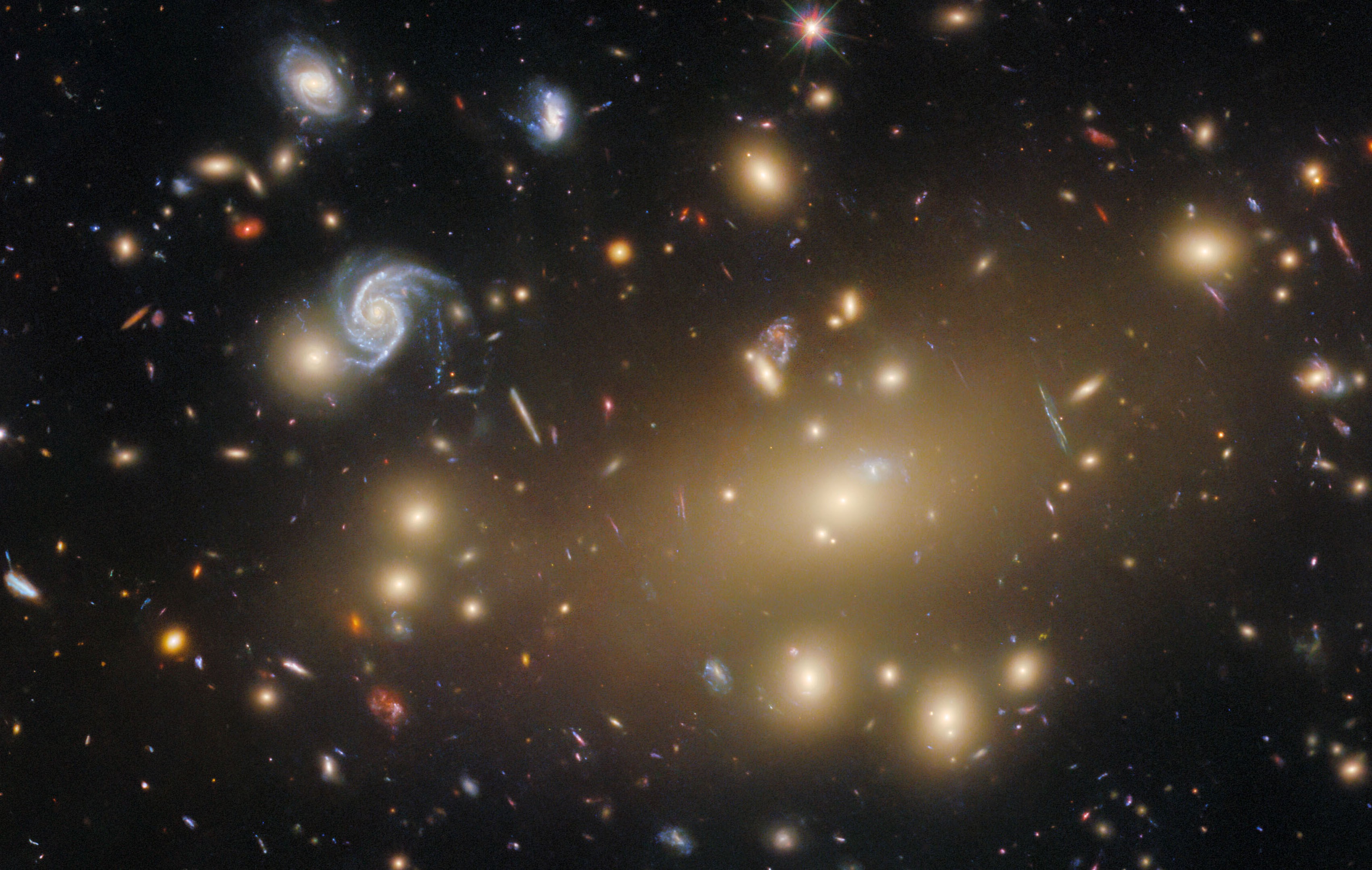 About a hundred galaxies of varying shapes and sizes, some of them appearing stretched and warped