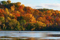 A person sits in a canoe on a lake surrounded by fall-colored trees.