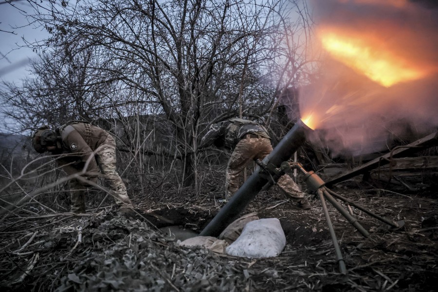 Ukrainian soldiers fire a mortar round, which creates a visible cone of smoke and fire as it leaves the tube.
