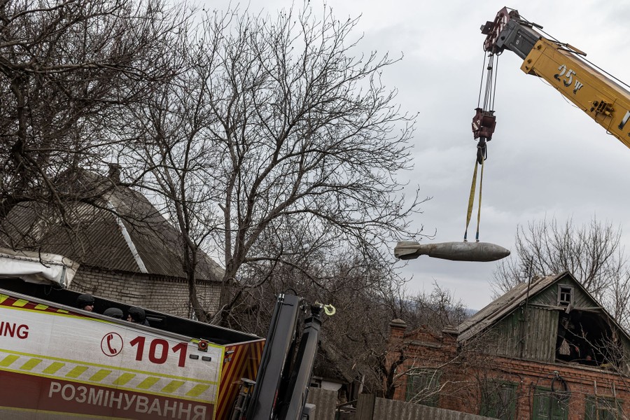 A crane lifts a large unexploded bomb out of a damaged house.
