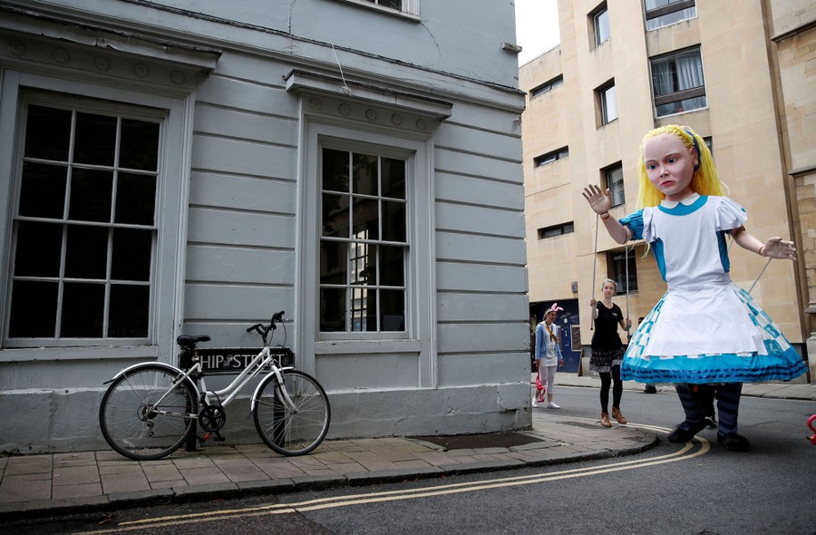 A large marionette of Alice (from "Alice's Adventures in Wonderland") walks through a city street.