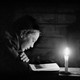 A black-and-white photo of a young boy reading by candlelight