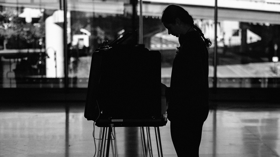 A photo of a voter in silhouette using a voting booth at a polling station