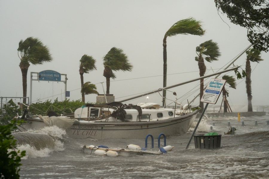 Windblown palm trees and crashing waves around a damaged sailboat