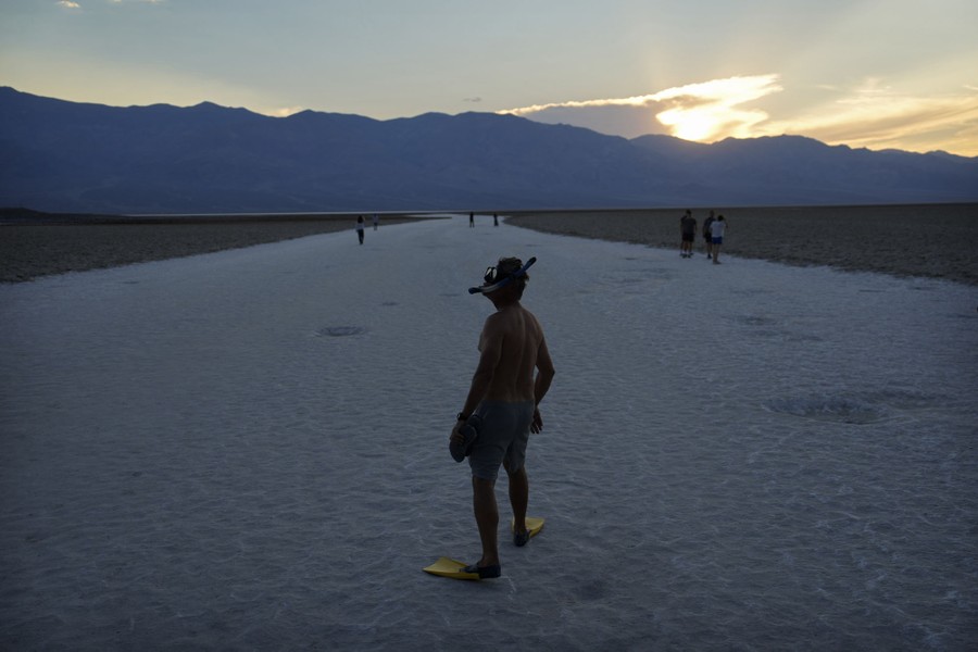 A person stands on a desert salt flat while wearing a diving mask, snorkel, and swim fins.