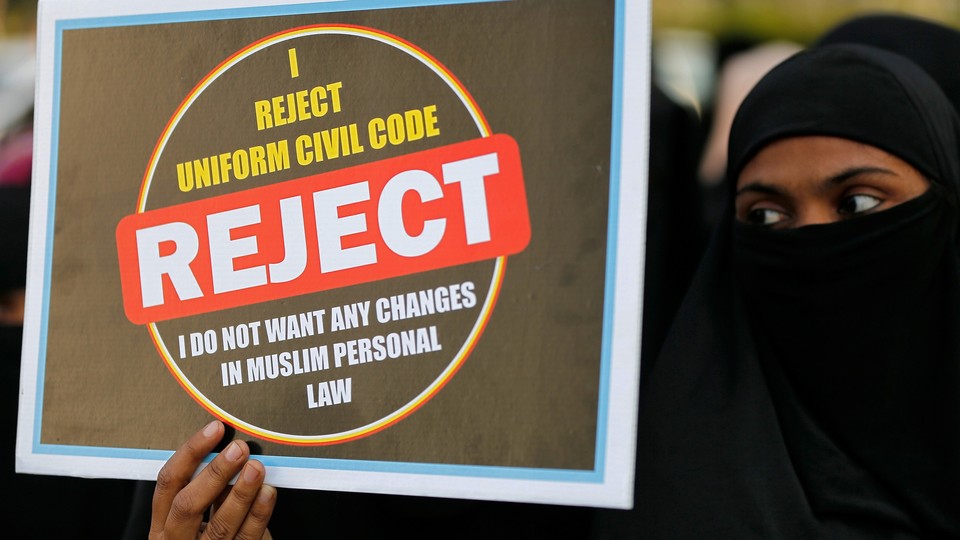 A woman in a niqab holds a placard reading "I reject uniform civil code. I do not want any changes in Muslim personal law."