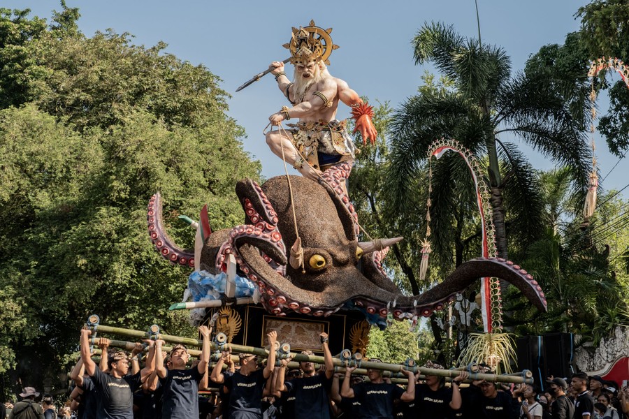 A group of people carry a large sculpture of a creature riding a giant octopus.