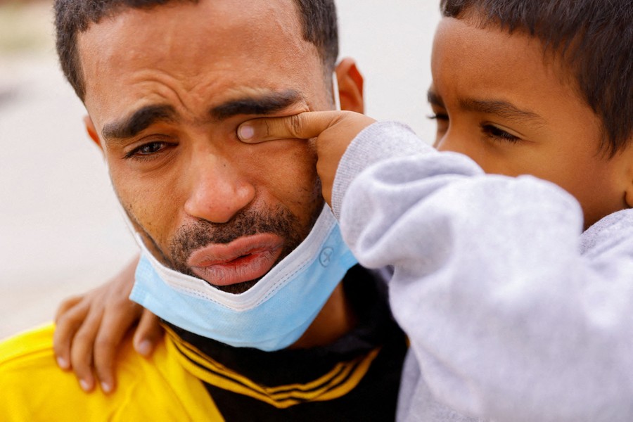 A young child uses his finger to wipe tears from the eyes of his father.