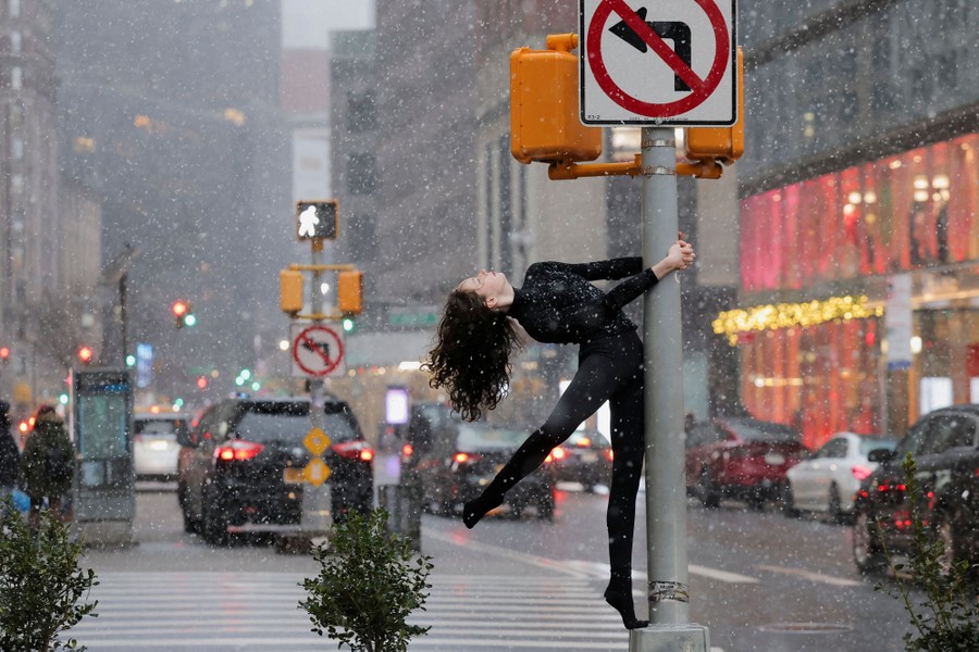 A person poses, hanging from a traffic pole, in New York City during a snowfall.