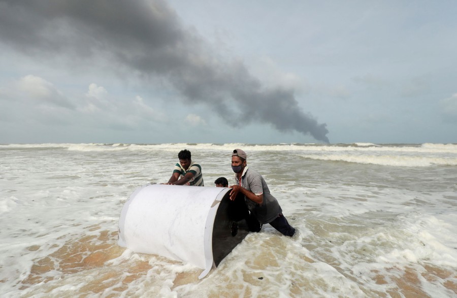Several people push a large piece of debris in the surf.