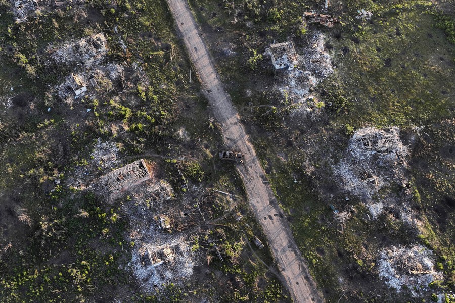 An aerial view of destroyed houses and an armored vehicle, in a war zone