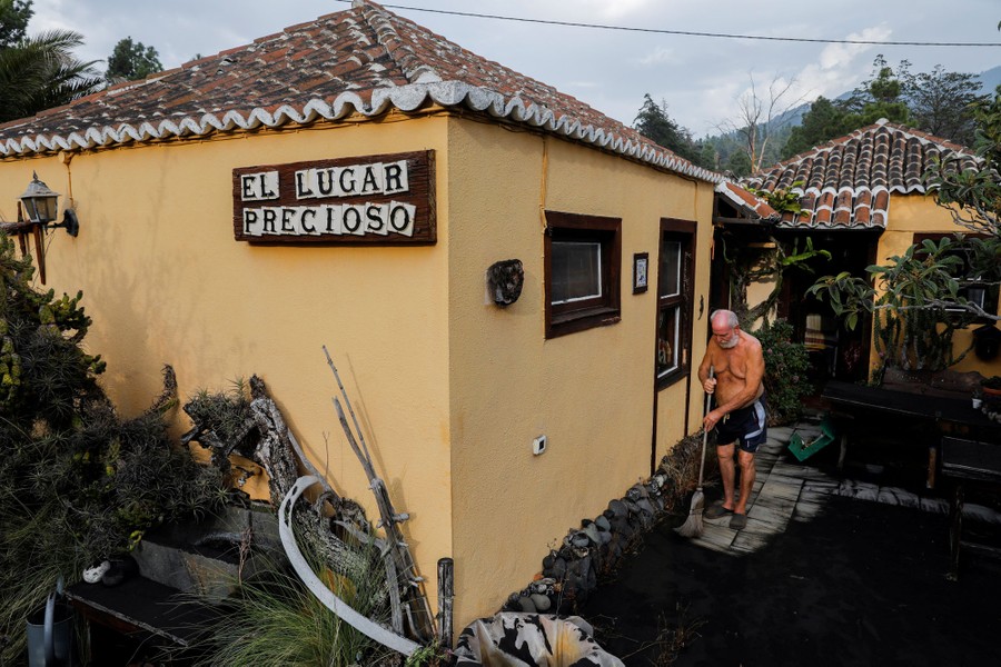 A man sweeps ash from pavement in front of a house.