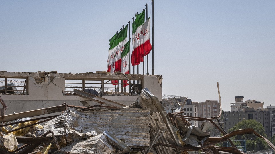 A color photo of Iranian flags flying above a bomb-damaged building.