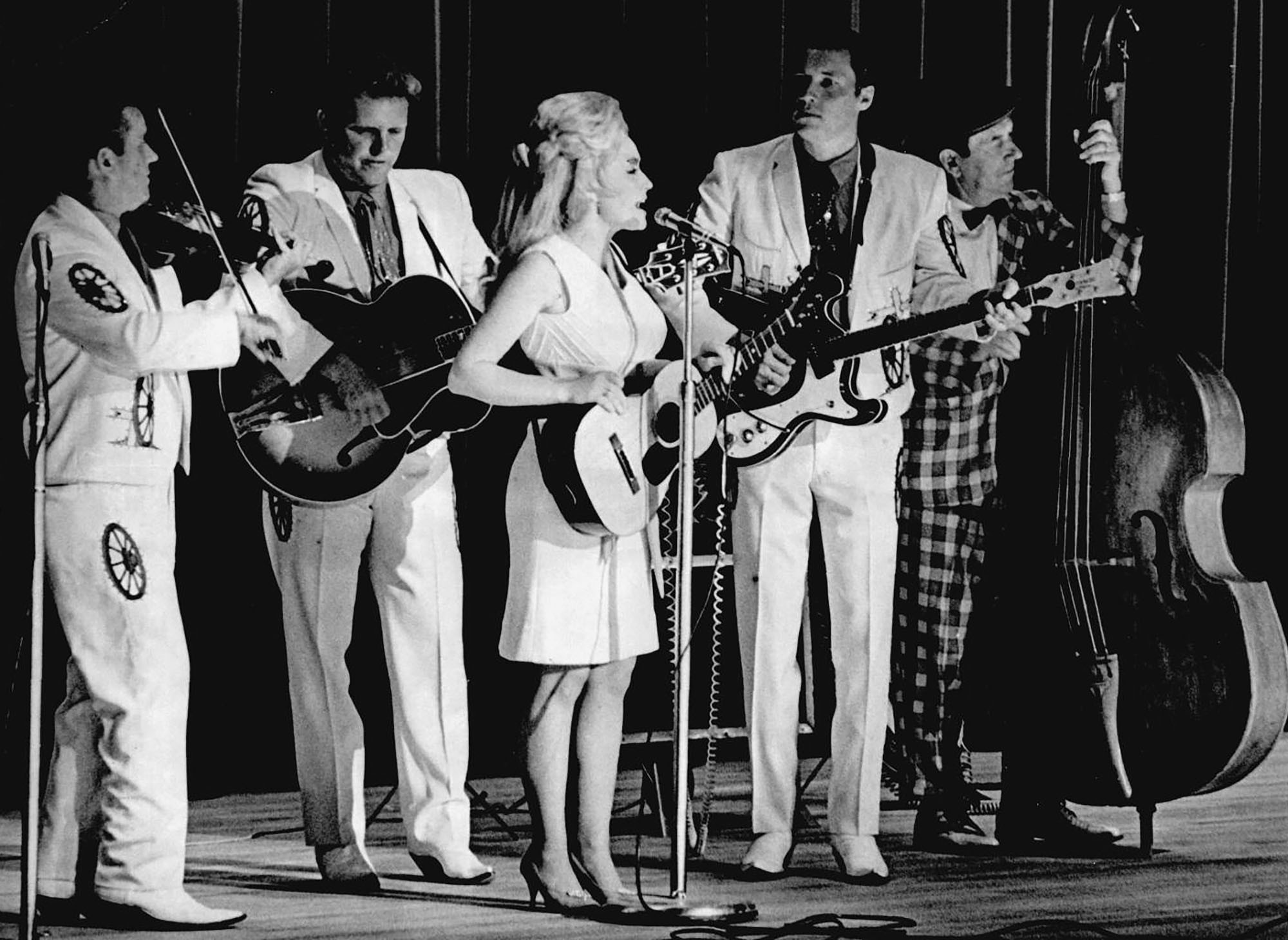 Dolly Parton performs onstage with a group of four other musicians.