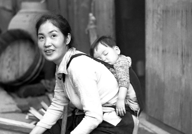 Woman crouching down with a sleeping baby strapped to her back