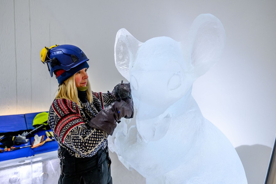 An artist carves a large rat out of blocks of ice.