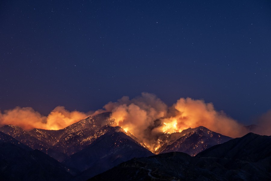 A distant view of mountainsides covered in embers and flames, seen at night