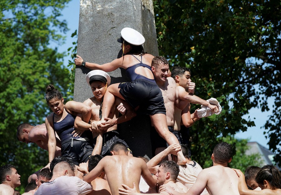 A group of students form a human pyramid to scale a slippery stone monument.