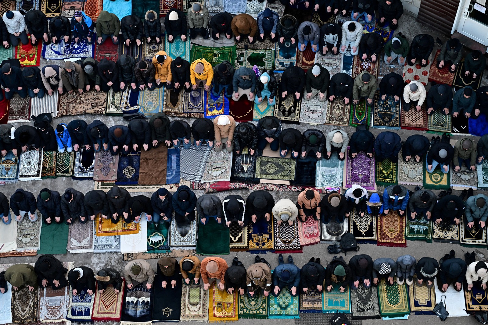 An aerial view of Muslim men kneeling on prayer mats arranged in rows.