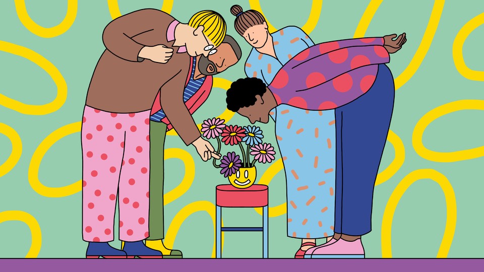 A group of people leaning over to admire a bouquet of flowers in a smiley vase