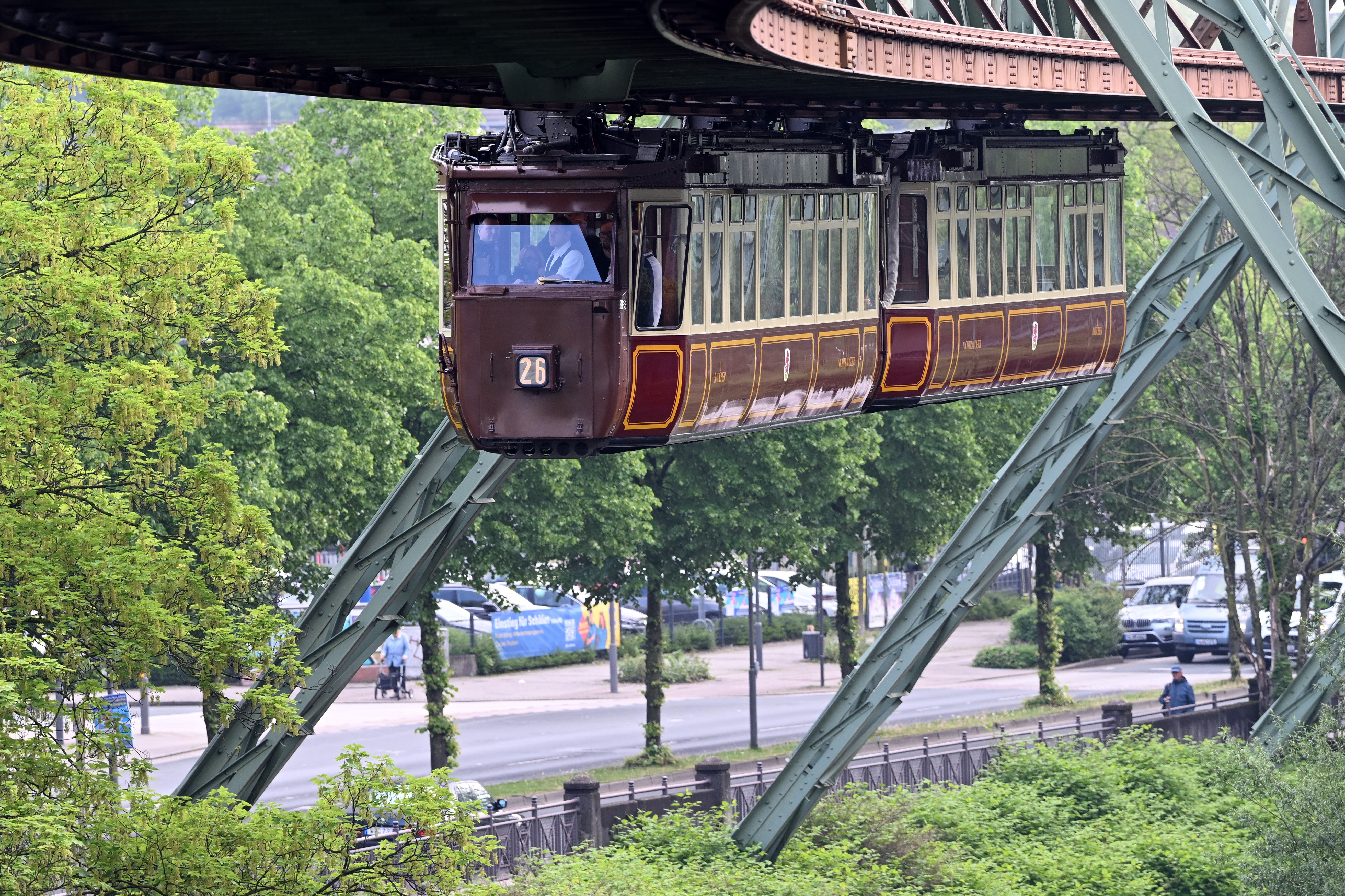 A historic suspension rail car travels along beneath an elevated track.