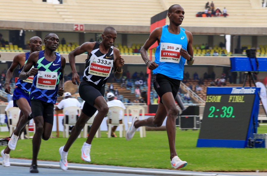 Several runners round a bend during a race in a stadium.