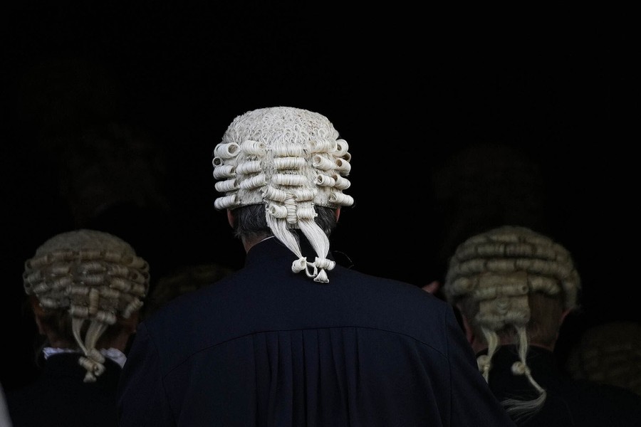 The backs of three British judges are seen as they walk into a building, each wearing a traditional white wig.