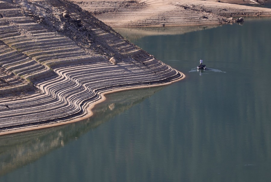 A person boats in a reservoir where the water level is very low.