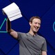 Mark Zuckerberg holds a stack of papers aloft, against a blue background.