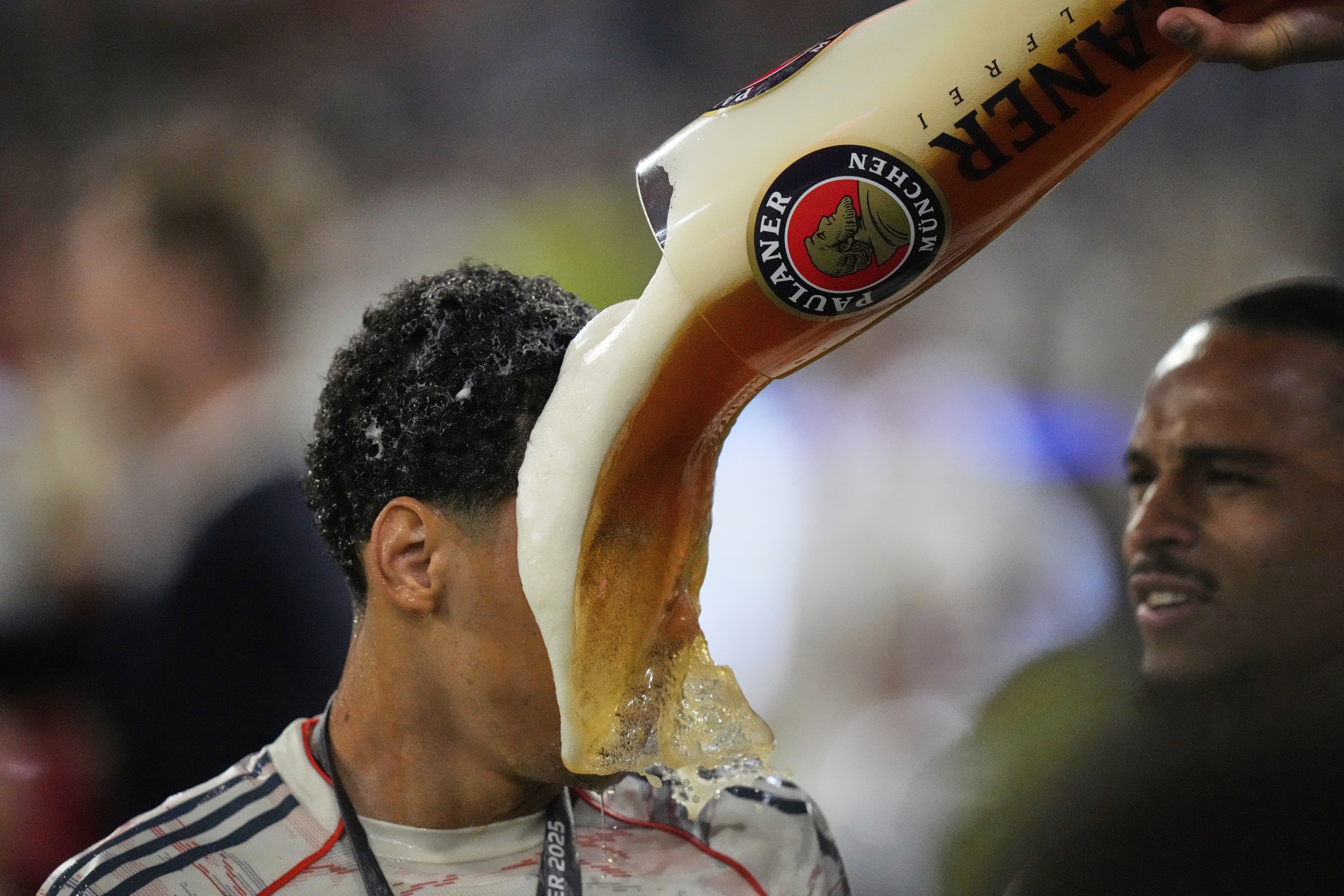 A soccer player has a large glass of beer poured on his face after a game.