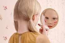 A young girl puts on lipstick in the mirror.