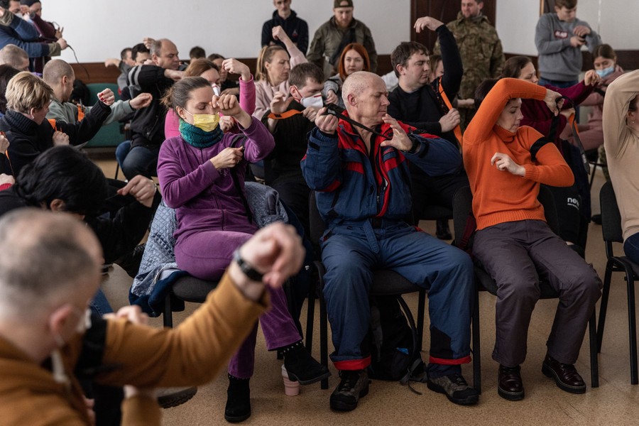 People sit in chairs in a room, practicing the use of tourniquets.