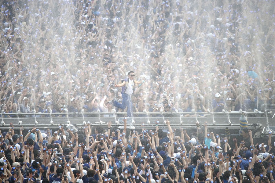 A performer runs on a long stage amid many small water jets and a huge crowd of fans.