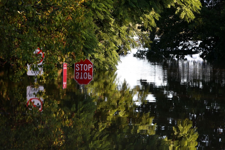 A mostly submerged stop sign is seen in a flooded intersection.