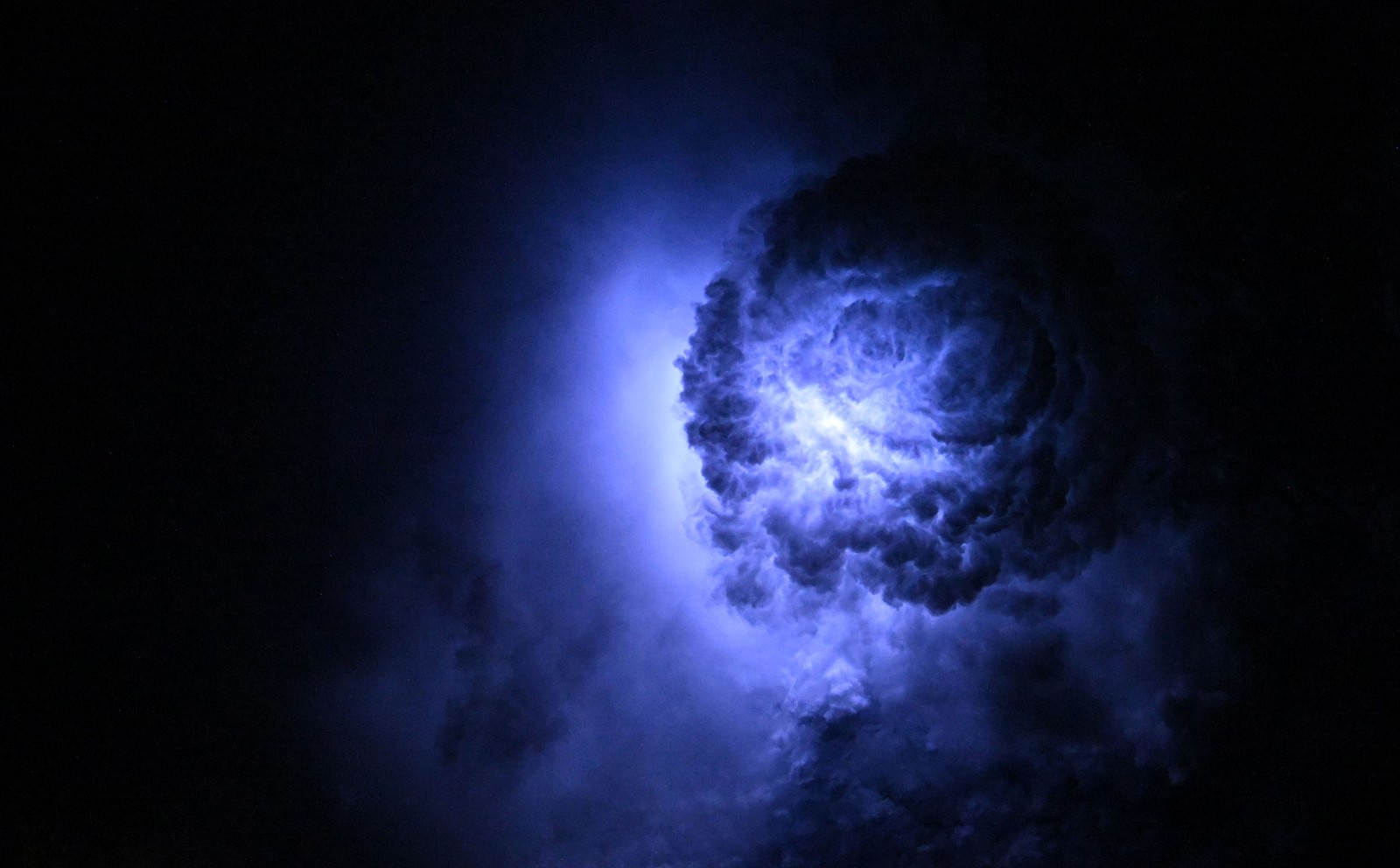 Lightning illuminates a storm cloud, seen from above.