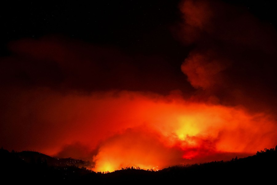 Flames illuminate rising smoke above a forest at night.