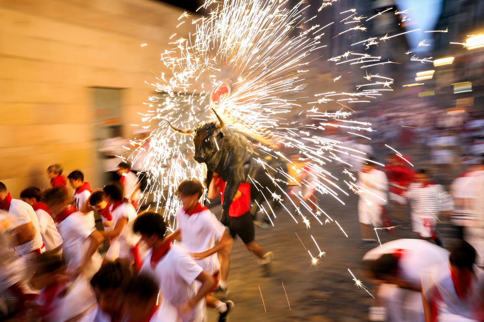 People react as the Fire Bull, a man carrying a bull figure packed with fireworks, runs by.