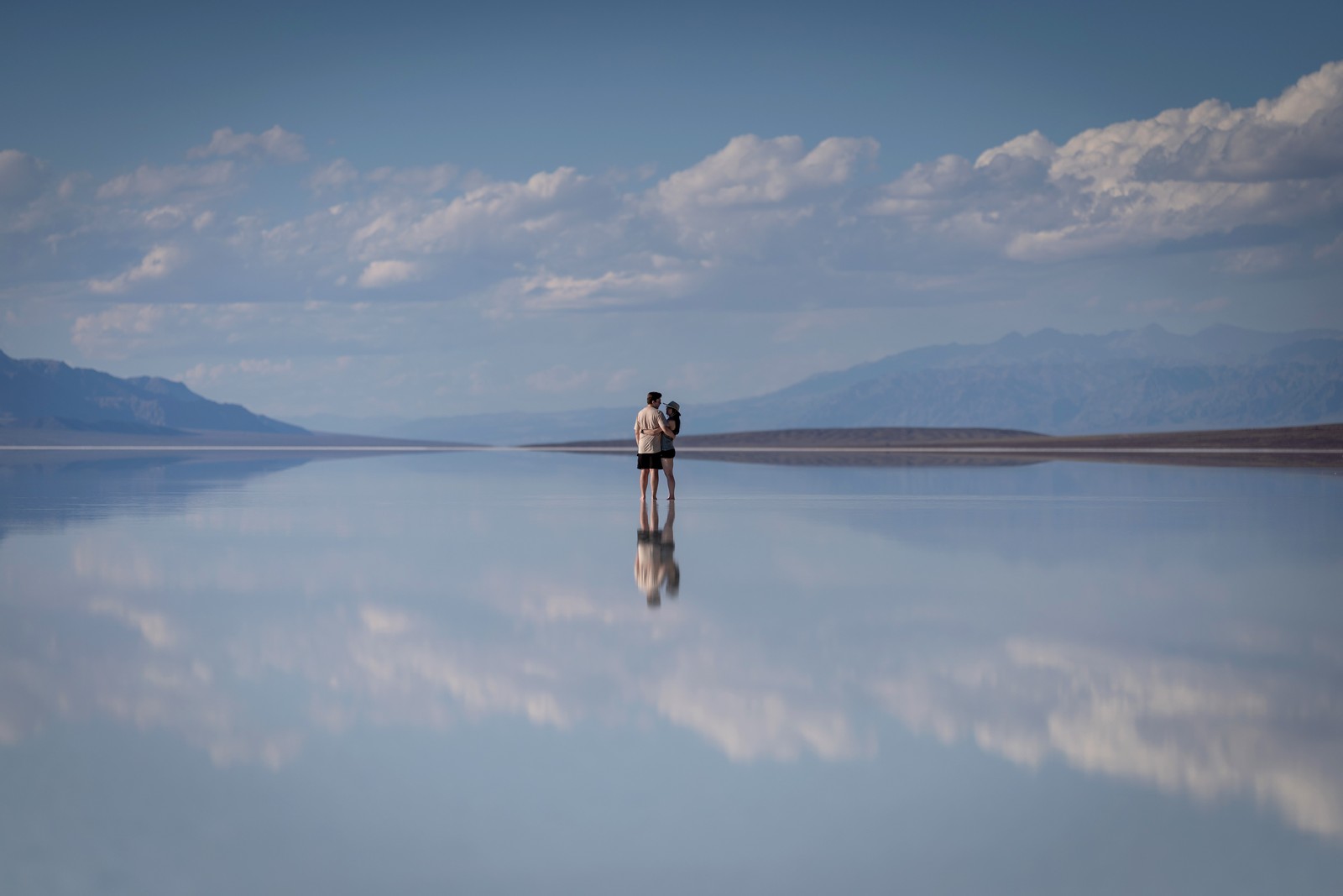A couple stands in very shallow water on a broad, flat plain in Death Valley.