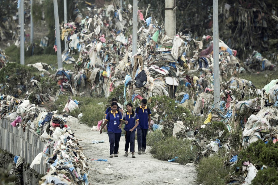 Several children walk on a path past huge piles of garbage left behind after floodwaters receded.