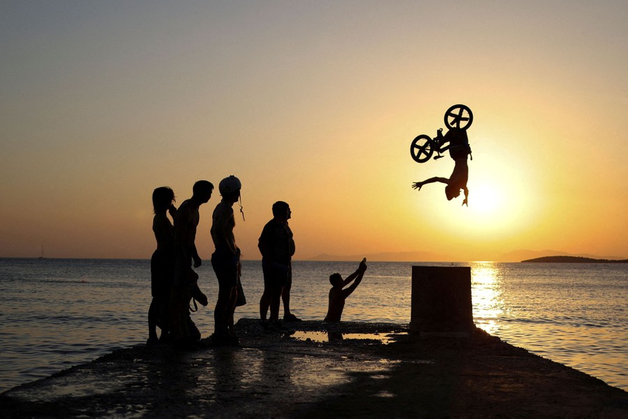 A person rides a bike off a ramp on a pier as several others watch.