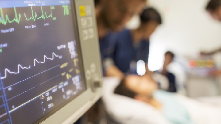 A monitor displays EKG readings while doctors attend a patient.
