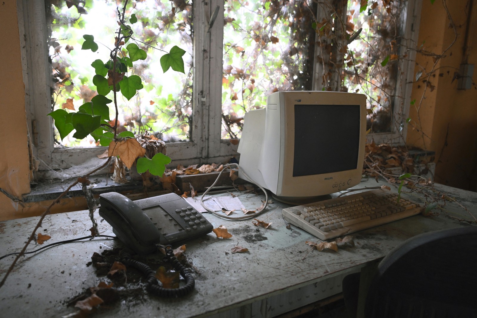 Vines grow across a dusty desk with an abandoned computer monitor and telephone.