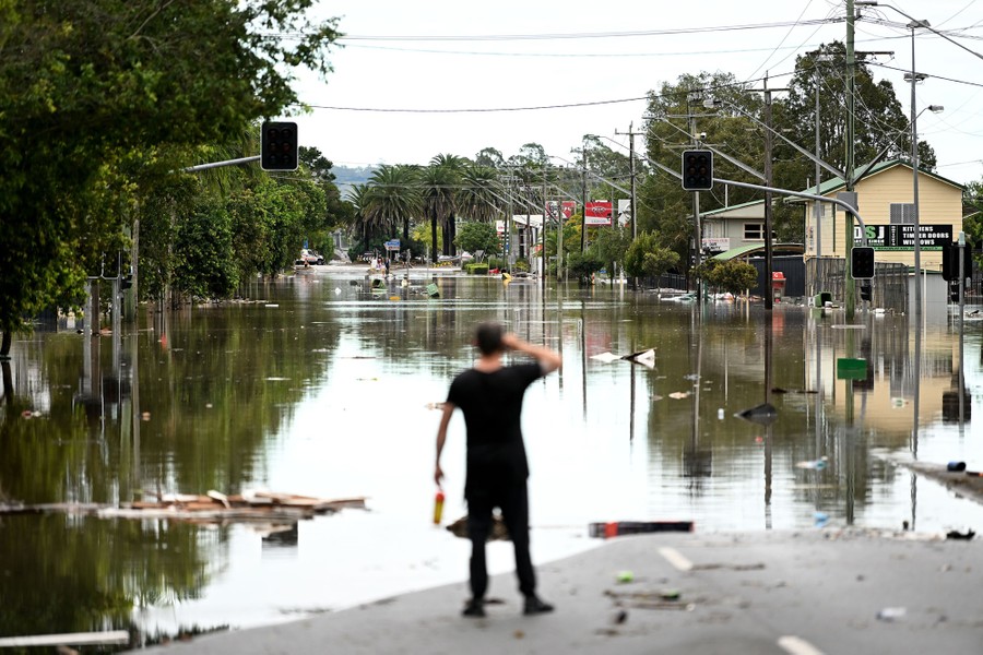 A person stands at the edge of the water on a flooded street.