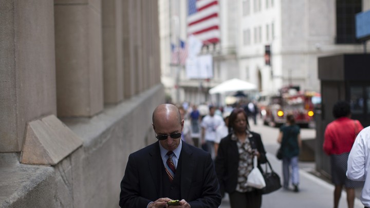 A man checks his phone while walking down a busy street